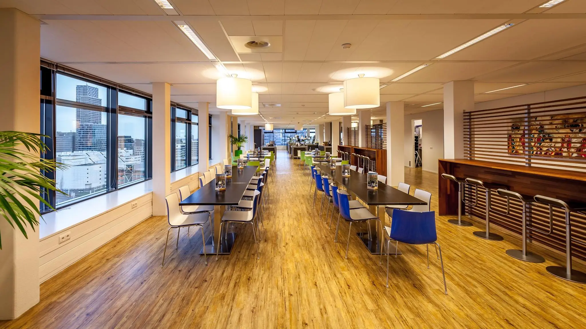 Moderne bedrijfskantine aan de Prinses Beatrixlaan met lange eettafels, kleurrijke stoelen en uitzicht op Den Haag.